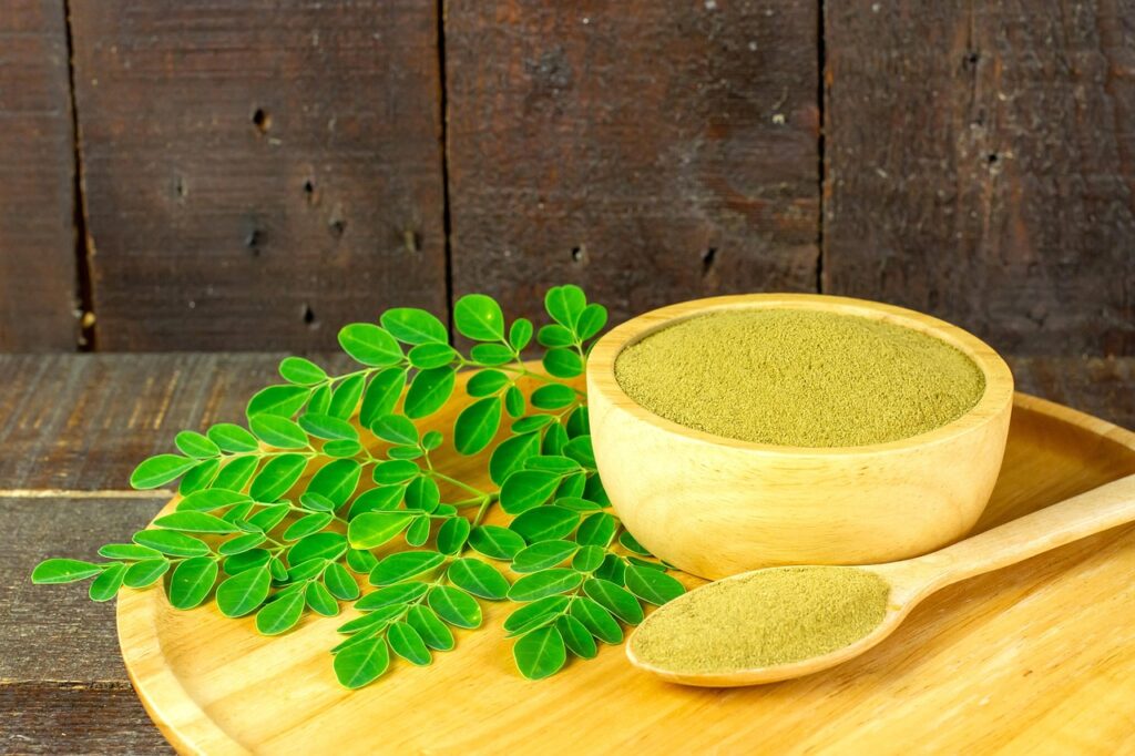 Moringa powder and fresh moringa leaves on wooden plate – natural remedy showcasing the benefits of moringa for skin, glowing and youthful complexion.