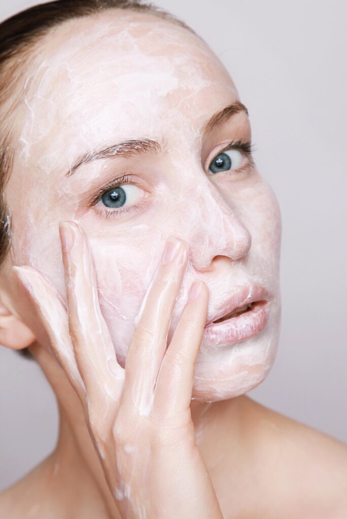 Woman applying exfoliator scrub to skin as part of essential skin care routine steps.